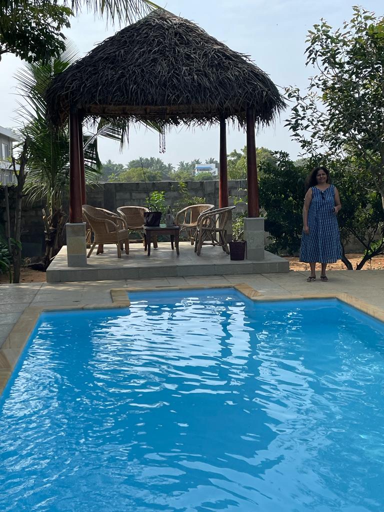 Blue swimming pool beside a thatched gazebo with wicker chairs and a guest