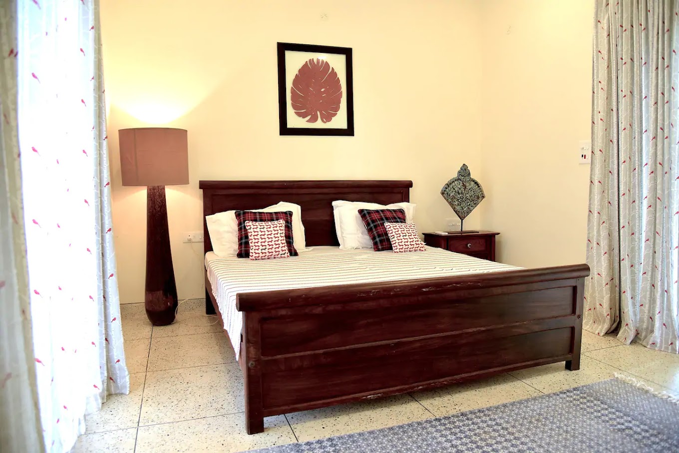 Wooden double bed with patterned cushions, a floor lamp and light curtains