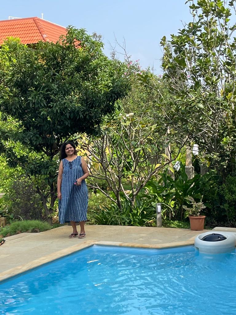 A guest beside the blue swimming pool surrounded by leafy tropical trees