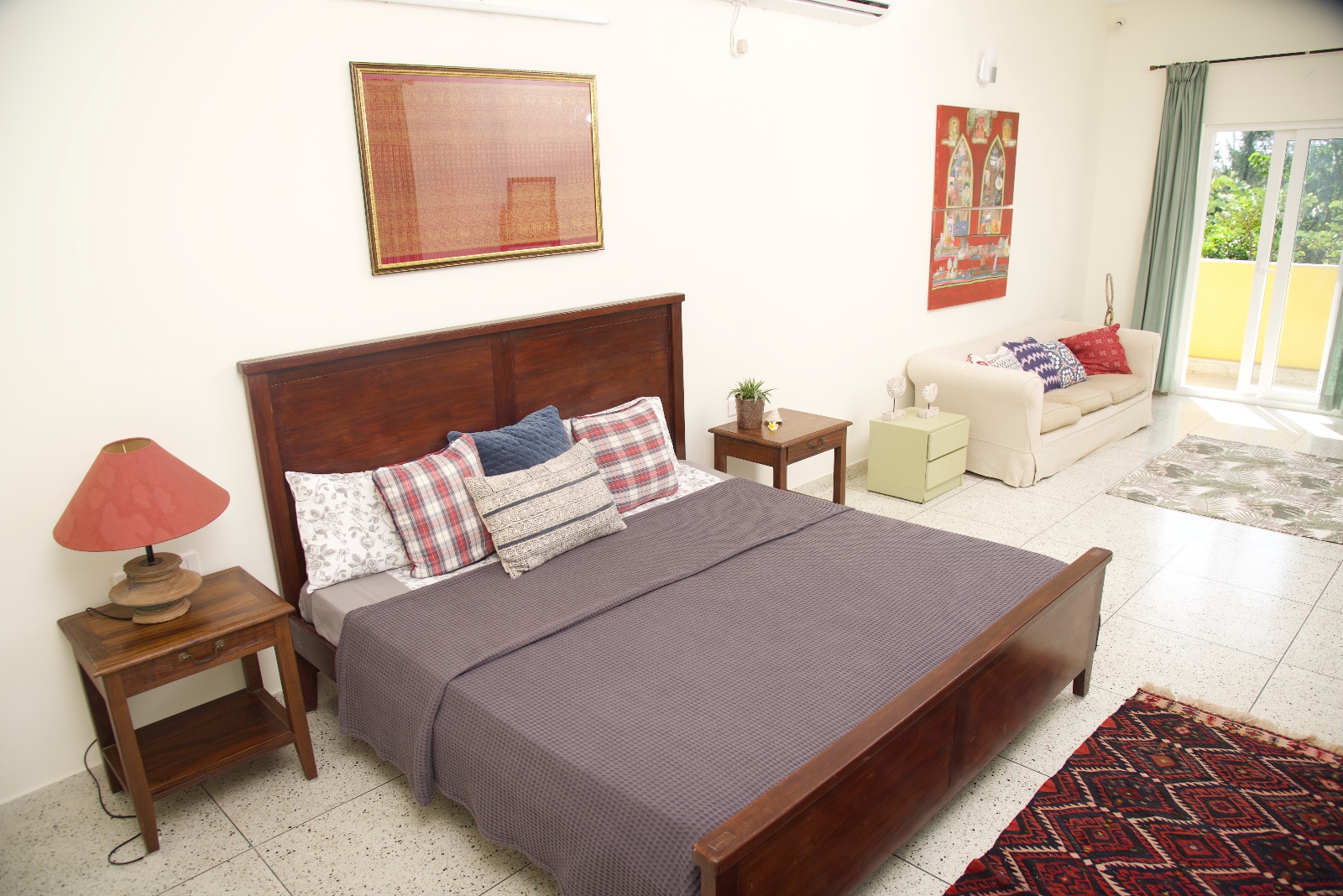Bright bedroom with a wooden double bed, bedside tables, a sofa and glass doors