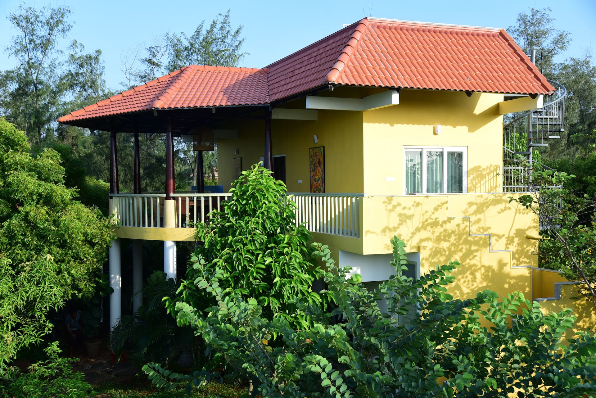 Villa 50 surrounded by lush gardens, with a red tiled roof and shaded veranda