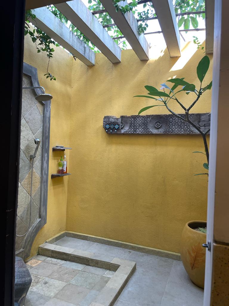 Open-air shower with yellow courtyard walls, overhead beams and leafy plants