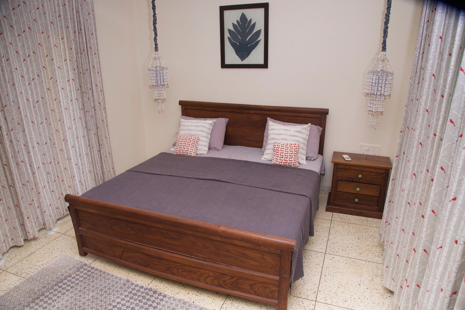 Wooden double bed with patterned pillows, beaded pendant lights and a framed leaf print
