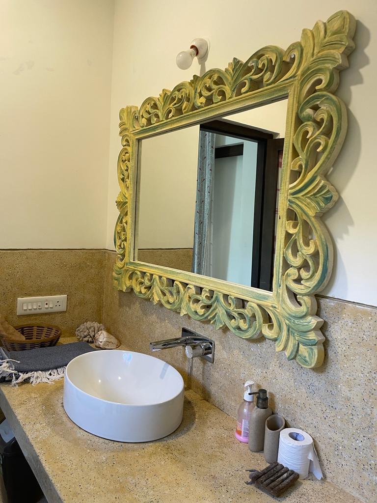 Bathroom vanity with a white basin and an ornate carved green mirror