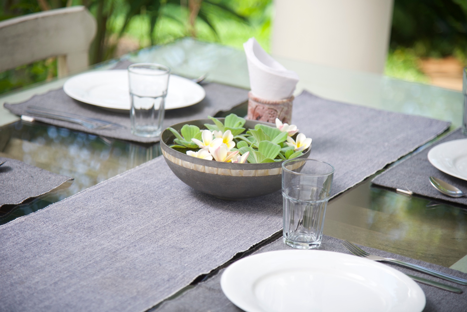 Glass dining table set with plates, glasses and a bowl of fresh flowers